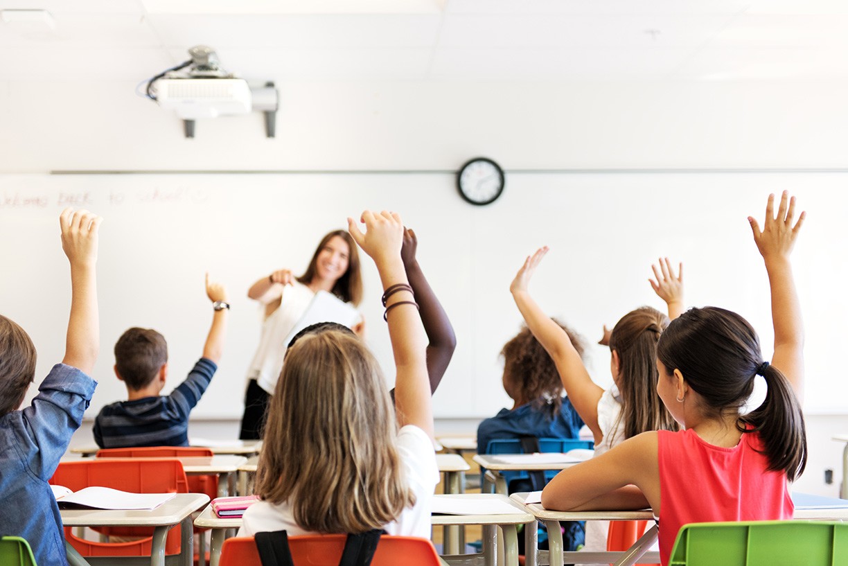 School kids in classroom raising hands