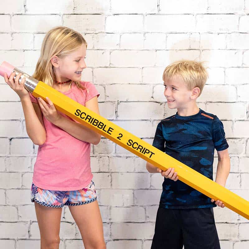 two kids holding a large pencil and smiling at each other.