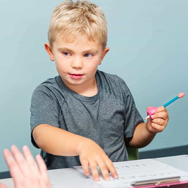 Young boy with glasses practicing handwriting on a whiteboard.