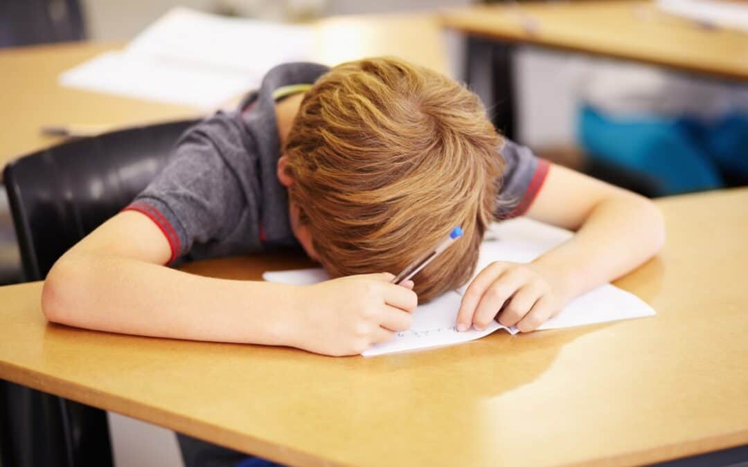 boy sleeping in classroom with head on his notebook