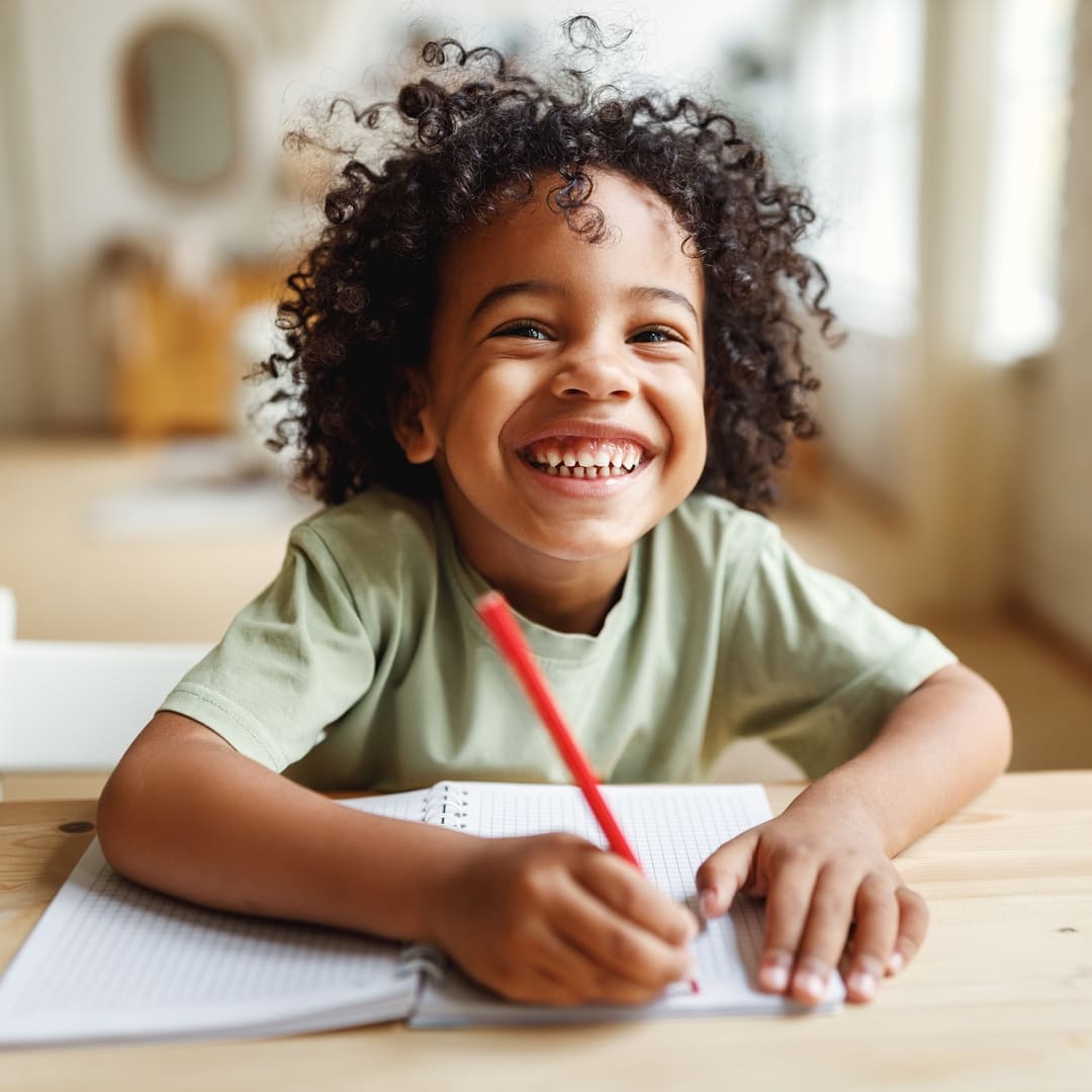 Smiling african american child school boy doing homework while sitting at desk at home